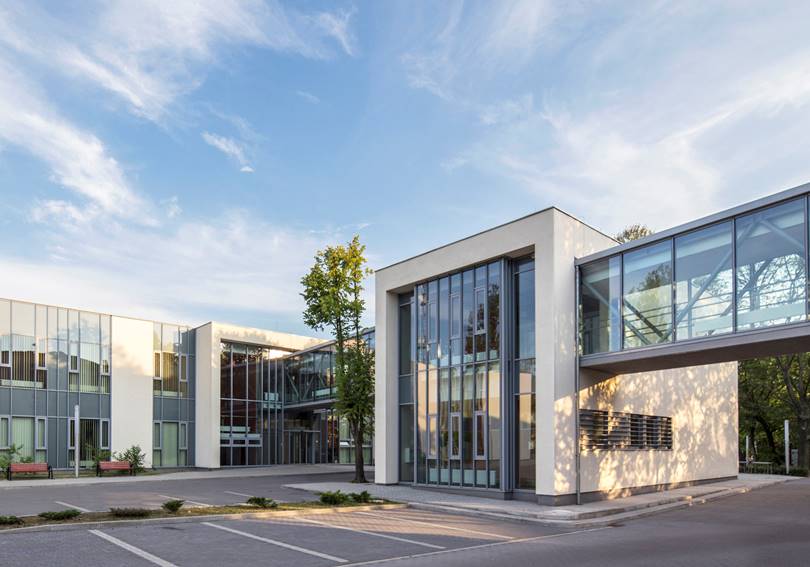 A glass-fronted building with a parking lot against the sky